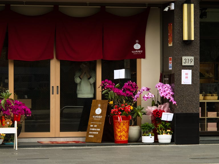 Colorful flowers adorn a shop entrance in Miaoli, Taiwan, creating a vibrant street scene.